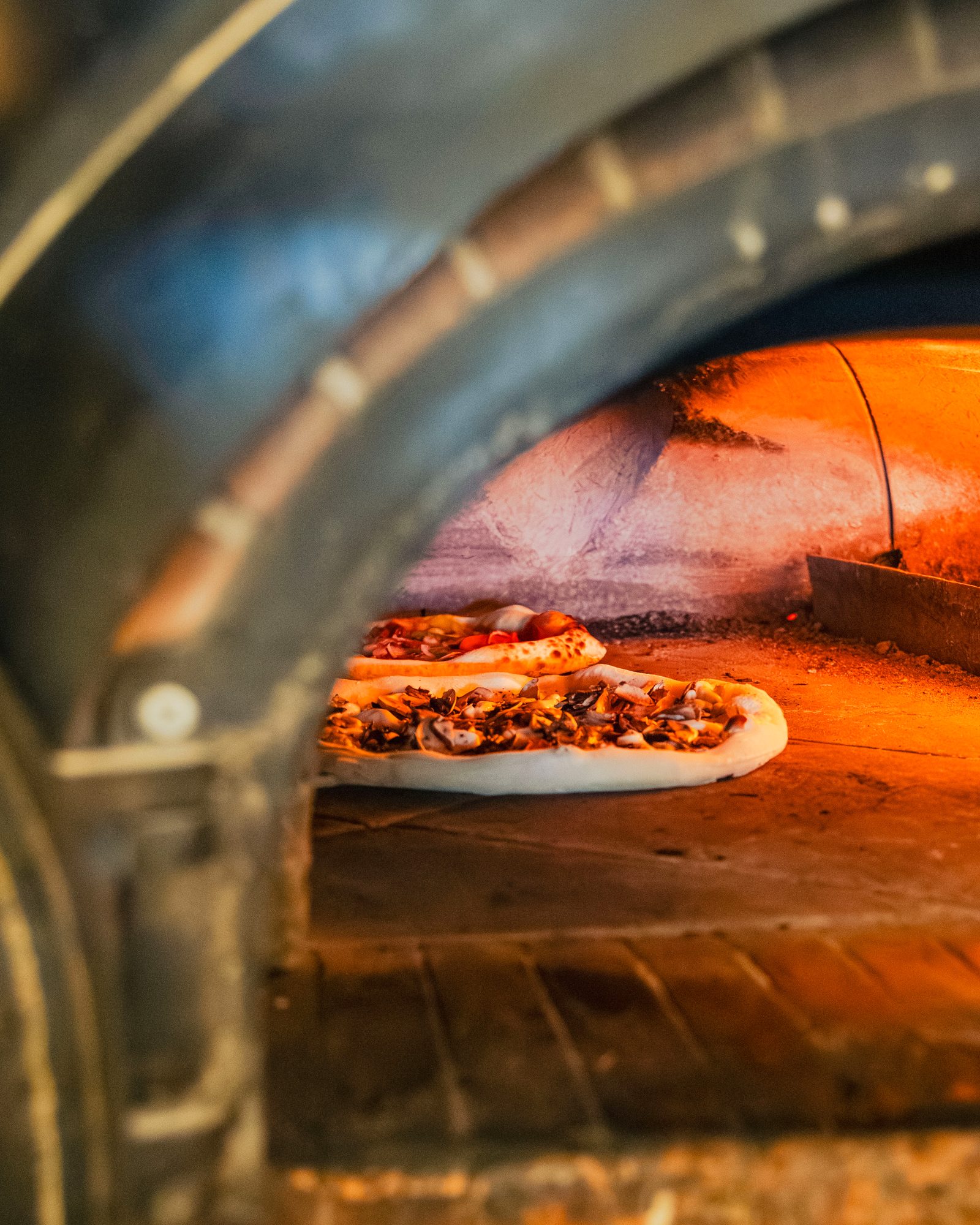 Une pizza glisse dans le four à bois de Pozzi Nonni, flammes au fond